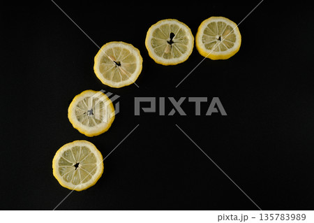 Five lemon slices lined up in a semicircle on a black background isolated 135783989