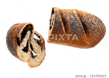 Ruddy loaf sprinkled with poppy seeds and stuffed with poppy seeds, roll, cut into pieces, on a white plate isolated 135784025