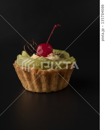 Fruit dessert cake with cherries, a leaf of chocolate, kiwi wedges and protein cream on a black background isolated Fruit dessert cake with cherries, a leaf of chocolate, kiwi wedges and protein cream on a black background isolated 135784086