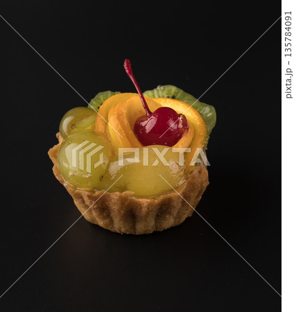 Fruit dessert cake with cherries, grapes sponges, kiwi slices and orange slices on a black background isolated 135784091