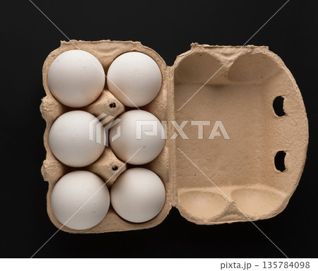 Chicken eggs, in the amount of six pieces in a disposable paper tray on a black background, isolated Chicken eggs, in the amount of six pieces in a disposable paper tray on a black background, isolated 135784098