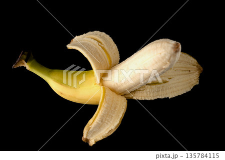 One ripe banana, half peeled, on a black background, isolated 135784115