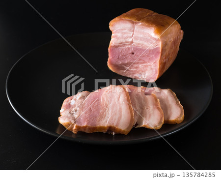 Food, a piece of bacon and cut into slices, on a black plate on a black background Food, a piece of bacon and cut into slices, on a black plate on a black background 135784285