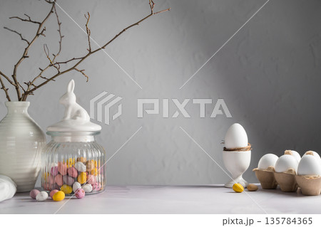 Easter background with mini egg candies in a jar, twigs in a vase and white chicken eggs 135784365