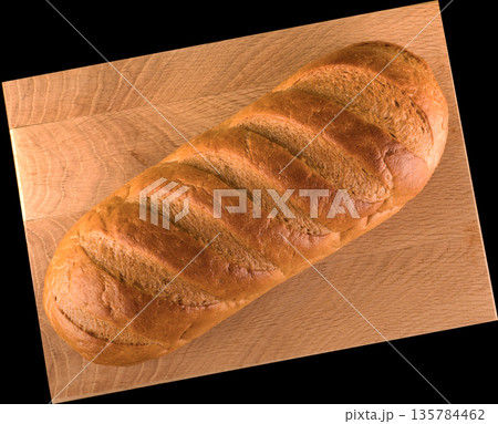 Ruddy whole loaf of bread on wood board on black background 135784462
