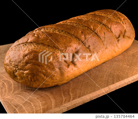 Whole loaf of bread on a wooden board, on a black background 135784464