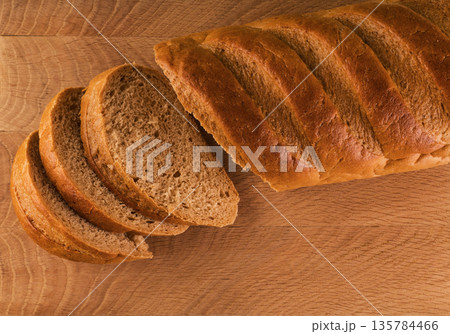 Loaf of bread and slices cut from it laid on a wooden board 135784466