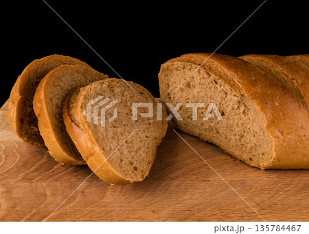 part of a loaf of bread and slices cut from it, laid on a wooden board, on a black background 135784467