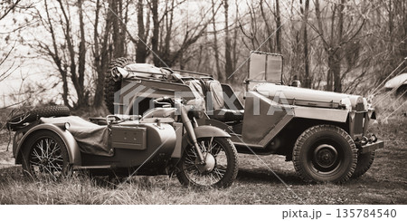 Old Tricar, Three-Wheeled Gray Motorcycle With A Sidecar Of German Forces and Willys Mb (jeep, U.s. Army Truck, 4x4) Parked At Forest During Reconstruction Of Some Fight World War II. Black and white 135784540