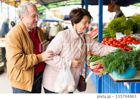 elderly man and woman buy radishes at an open market elderly man and woman buy radishes at an open market 135784863