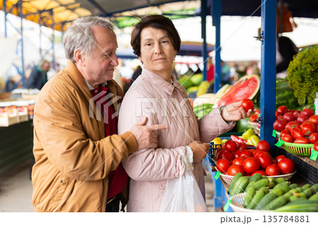 elderly man and woman buy tomatoes at an open market 135784881