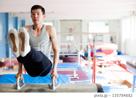 Male athlete doing complicated exciting trick on pommel horse in professional gym Male athlete doing complicated exciting trick on pommel horse in professional gym 135784882