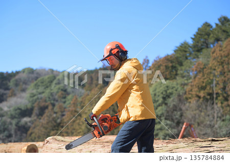 青空を背景にチェーンソーを構える日本人男性　撮影協力：多摩森林センター協同組合 135784884
