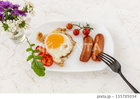 Fried egg and grilled sausages served with fresh tomatoes, sliced bell pepper on the plate. Fried egg and grilled sausages served with fresh tomatoes, sliced bell pepper on the plate. 135785034