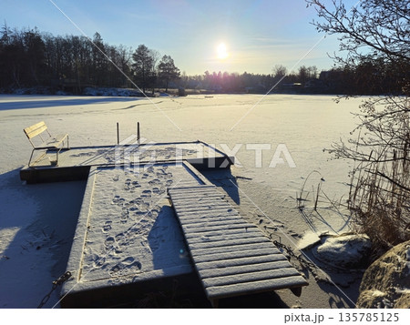 A pier and a bench on the frozen lake on a sunny winter. A pier and a bench on the frozen lake on a sunny winter. 135785125