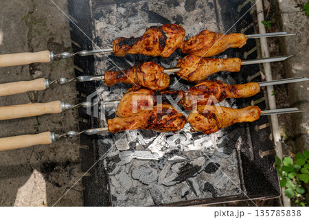 Chicken shanks on skewers on grill, grilling. 135785838