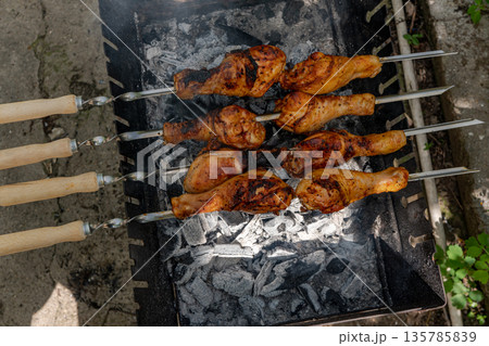 Chicken shanks on skewers on grill, grilling. 135785839