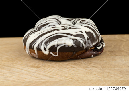 bun covered with chocolate, on a wooden board, on a black background 135786079