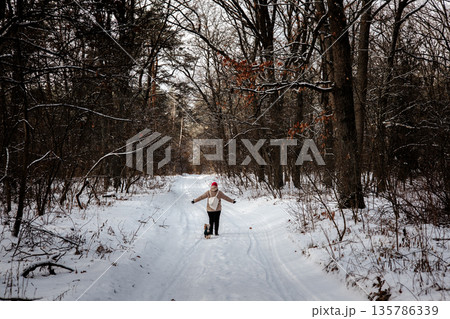 A person with outstretched arms enjoys a moment of peace on a snowy forest path. This authentic lifestyle image captures a sense of freedom, winter exploration, and serene solitude in nature. 135786339