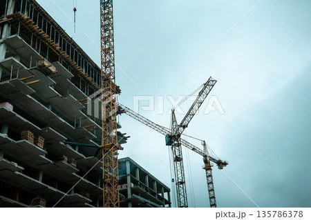Urban construction of a high-rise building with tower cranes against an overcast sky. Modern architecture, industry, urban growth themes. Real estate. Urban construction of a high-rise building with tower cranes against an overcast sky. Modern architecture, industry, urban growth themes. Real estate. 135786378