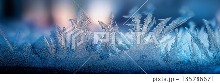 Frosty ice crystal patterns forming on blue glass. Blue frosty ice forming sharp, sparkling crystal patterns on a cold surface 135786671