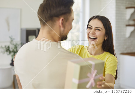 Young happy smiling woman holding present gift box and hugging her boyfriend at home 135787210