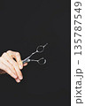 Hand of hairdresser or hairstylist holding professional shears isolated on black background 135787549