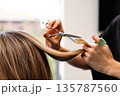 Professional hairstylist trimming hair female client with scissors, close-up view of hands shaping smooth strands inside modern beauty salon with natural light 135787560