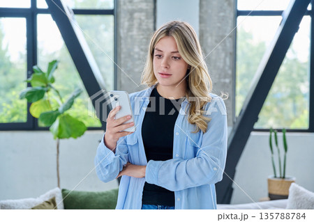 Young woman standing at home using smartphone 135788784