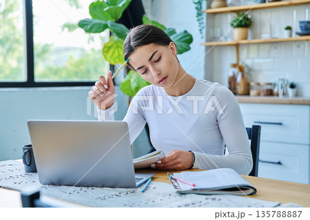 Teenage girl student sitting at the table with laptop, textbooks in home interior 135788887