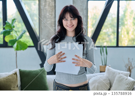 Smiling young woman with business study important papers standing in home interior Smiling young woman with business study important papers standing in home interior 135788916