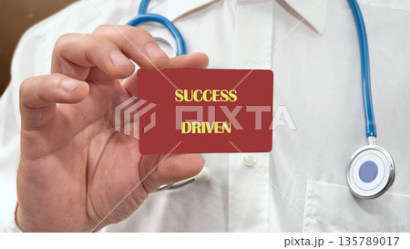 A person in a white lab coat and blue stethoscope holds a red card at chest height 135789017