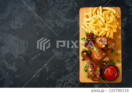 Grilled chicken drumsticks with ketchup and french fry on a black table, top view. 135790159