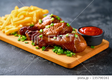 Grilled chicken drumsticks with ketchup and french fry on a black table. Grilled chicken drumsticks with ketchup and french fry on a black table. 135790161