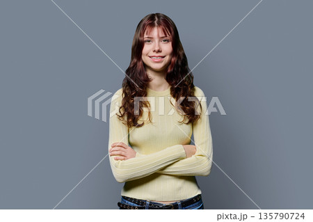 Portrait of smiling confident teenage girl with crossed arms on gray background 135790724