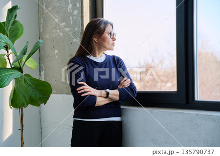 Middle-aged confident serious woman looking at window Middle-aged confident serious woman looking at window 135790737