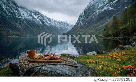 Breakfast pastries and coffee sit by a majestic mountain lake 135791003