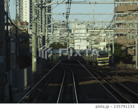 都会のビル群を背景に線路を走るJR通勤電車。複雑な架線とカーブを描くレールの都市鉄道風景 都会のビル群を背景に線路を走るJR通勤電車。複雑な架線とカーブを描くレールの都市鉄道風景 135791133