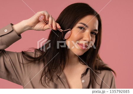 Charming Woman Doing Face Massage With Rose Quartz Stone Roller For Firmer 135792085