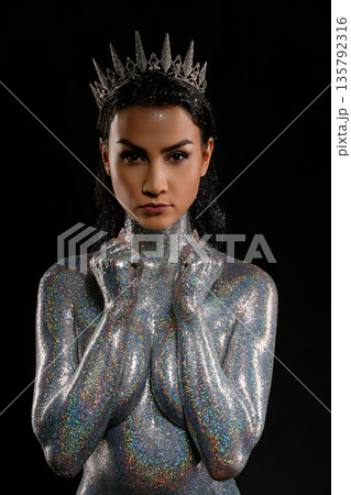Intense portrait of a fantasy queen covered in silver holographic glitter and wearing a crown. Intense portrait of a fantasy queen covered in silver holographic glitter and wearing a crown. 135792316