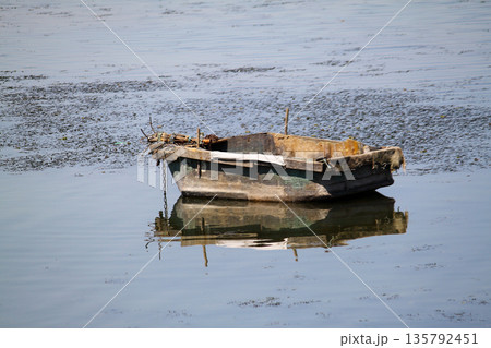 lonely fishing boat docked in calm lake. wooden fishing boat in a still lake water. image of wooden fishing boat moored on the shore. space for text. 135792451