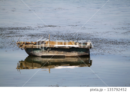 lonely fishing boat docked in calm lake. wooden fishing boat in a still lake water. image of wooden fishing boat moored on the shore. space for text. 135792452