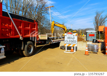 Workers manage construction on road with large machines, barriers during rural location. 135793267