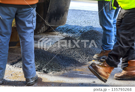 Workers handle asphalt material on road as they prepare for paving work during road repair, 135793268