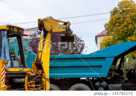 Construction machine uses its arm to load gravel into truck on worksite in city Construction machine uses its arm to load gravel into truck on worksite in city 135793273