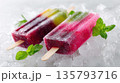 Two vibrant fruit popsicles are chilling on a bed of crushed ice with mint leaves 135793716