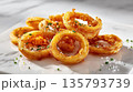 Crispy onion rings are piled on a white marble surface, ready to eat 135793739