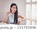 Charming young Asian woman holding a pencil while thinking when looking outside window in office. 135793896