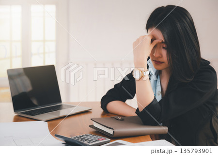 Young asian woman architect holding forehead while working on project at office desk. She is tired and tired. 135793901