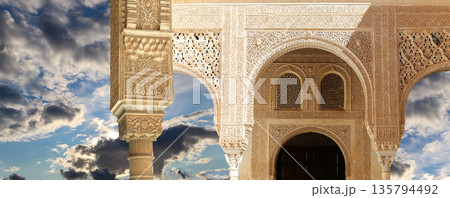 Arches in Islamic (Moorish) style (against the background of a beautiful sky with clouds) in Alhambra, Granada, Spain Arches in Islamic (Moorish) style (against the background of a beautiful sky with clouds) in Alhambra, Granada, Spain 135794492